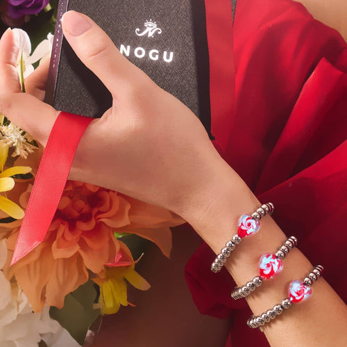 Crimson Swirl Glowing Heart Essence Bracelets with red and white heart beads and silver stainless steel beads worn on wrist holding NOGU box